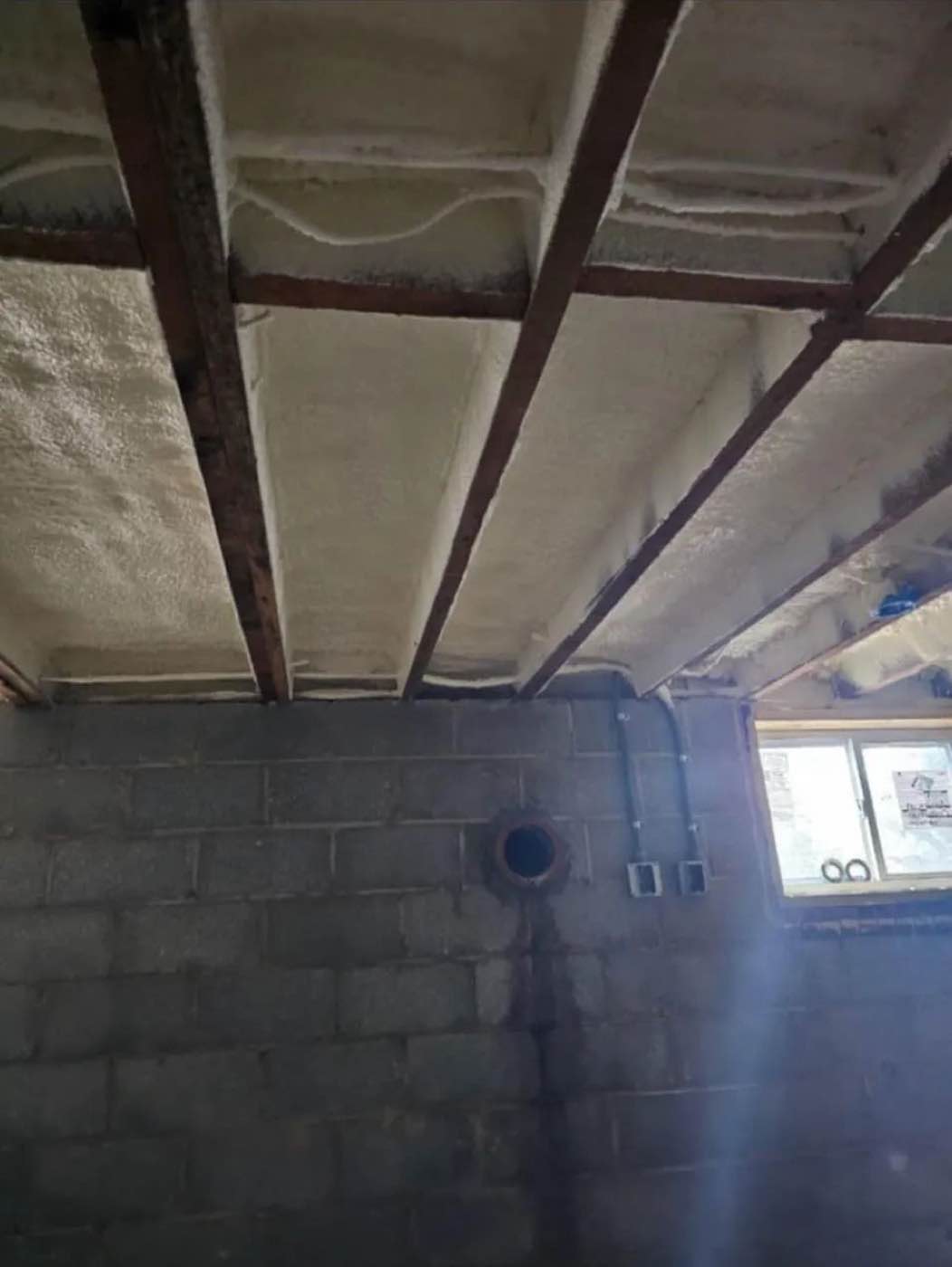 Crawl space floor joists insulated with spray foam above a block foundation wall
